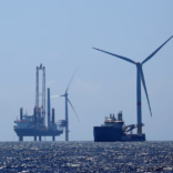 an image of a wind turbine in the ocean surrounded by a construction site and a large ship